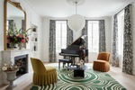 Living room with a grand piano, patterned green rug, and decorative chairs.
