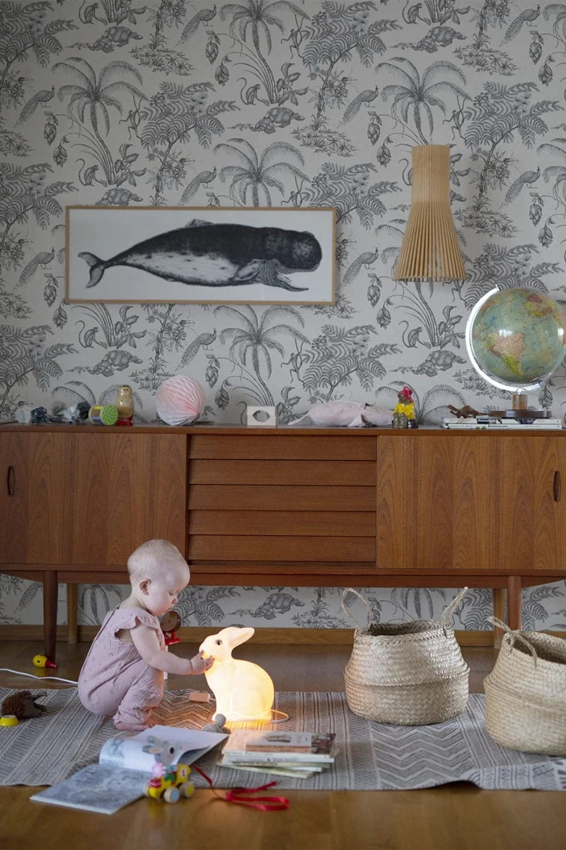 Child playing with toys on a rug in a room with wallpaper and furniture.