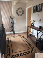 A beautifully styled living room featuring a handmade black scalloped jute rug. This area rug, perfect for a living room setting, sits elegantly on a wooden floor, accentuating the room's decor with its unique design. Ideal for a living room rug 8x10, this jute rug adds a touch of natural elegance to the space.