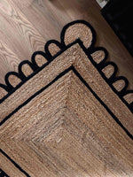 A stylish Handmade Black Scalloped Jute Rug, perfect for adding a touch of elegance to your living room. This area rug features a unique scalloped edge design in black, contrasting beautifully with the natural jute fibers. Ideal for living room rugs 8x10, this rug showcases intricate craftsmanship and blends seamlessly with wooden flooring.