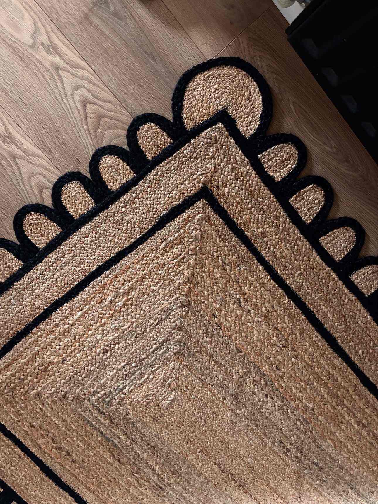 A stylish Handmade Black Scalloped Jute Rug, perfect for adding a touch of elegance to your living room. This area rug features a unique scalloped edge design in black, contrasting beautifully with the natural jute fibers. Ideal for living room rugs 8x10, this rug showcases intricate craftsmanship and blends seamlessly with wooden flooring.
