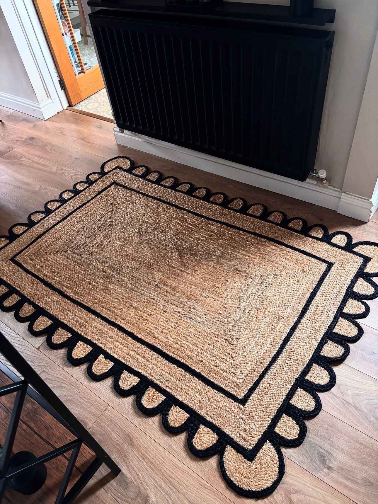 A beautifully crafted handmade black scalloped jute area rug placed in a living room. The natural fibers of the jute rug are accentuated by a striking black scalloped border, making it a perfect 8x10 addition to any living room space.