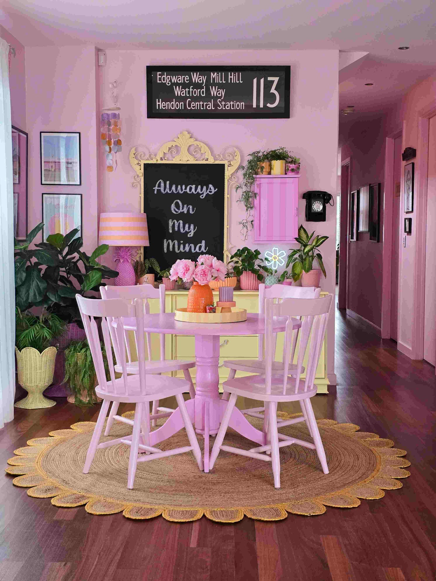 A cozy living room with a handmade yellow scalloped round jute rug beneath a pastel pink dining table set. The area rug adds a natural touch to the vibrant, pink-themed decor, creating a warm and inviting atmosphere ideal for any living room space.