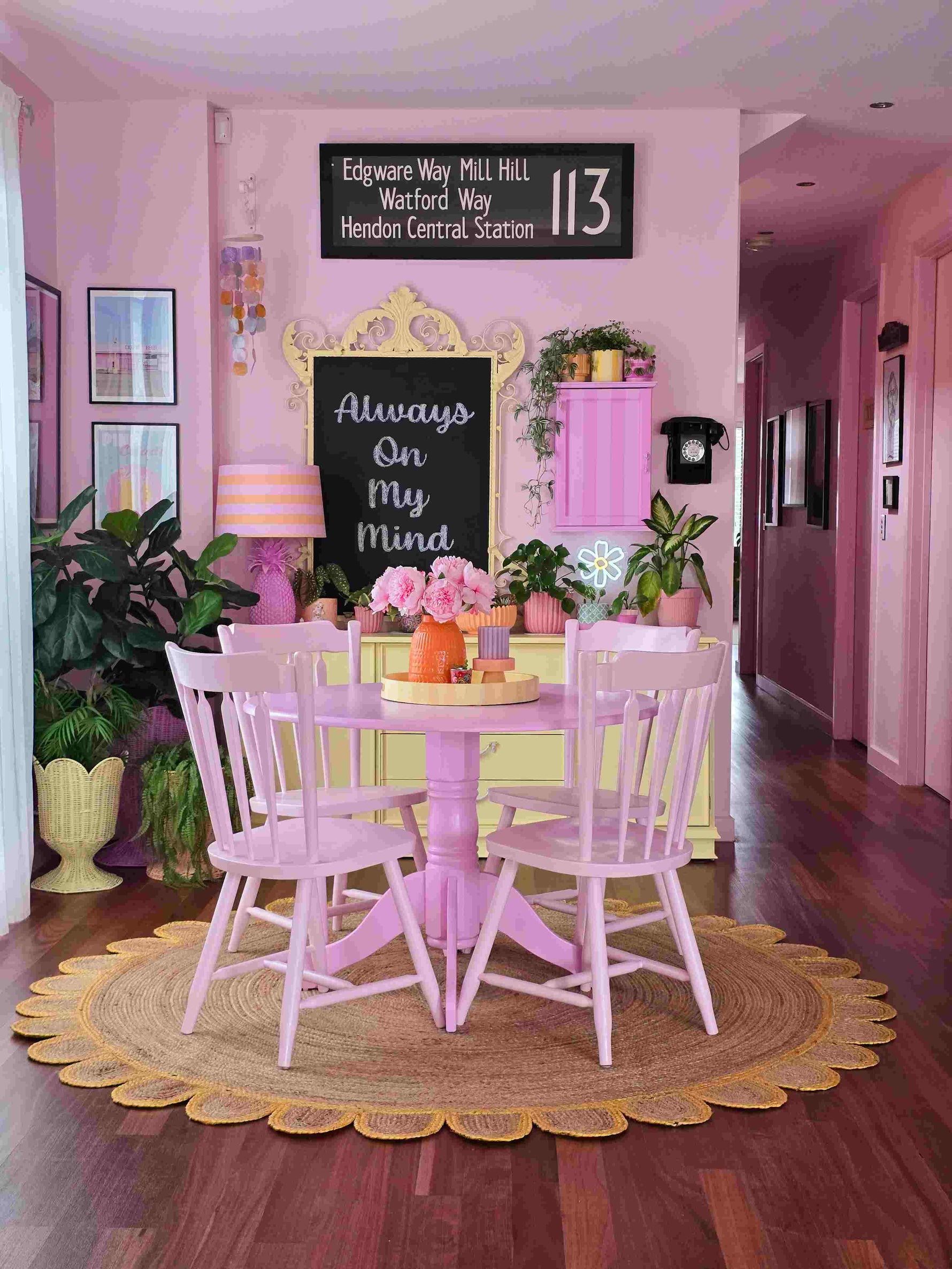 A cozy living room with a handmade yellow scalloped round jute rug beneath a pastel pink dining table set. The area rug adds a natural touch to the vibrant, pink-themed decor, creating a warm and inviting atmosphere ideal for any living room space.