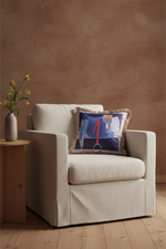 An olive green velvet sofa in a modern living room setting, styled with a decorative throw pillow and a small wooden side table holding a vase with dried branches.
