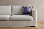 An olive green velvet sofa in a modern living room setting, styled with a decorative throw pillow and a small wooden side table with dried flowers.