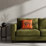 A white armchair with a light gray upholstered seat, styled in a room with a gray paneled wall, a wooden floor, a floor lamp, and a side table. The chair features a decorative green throw pillow with a gold horse design.