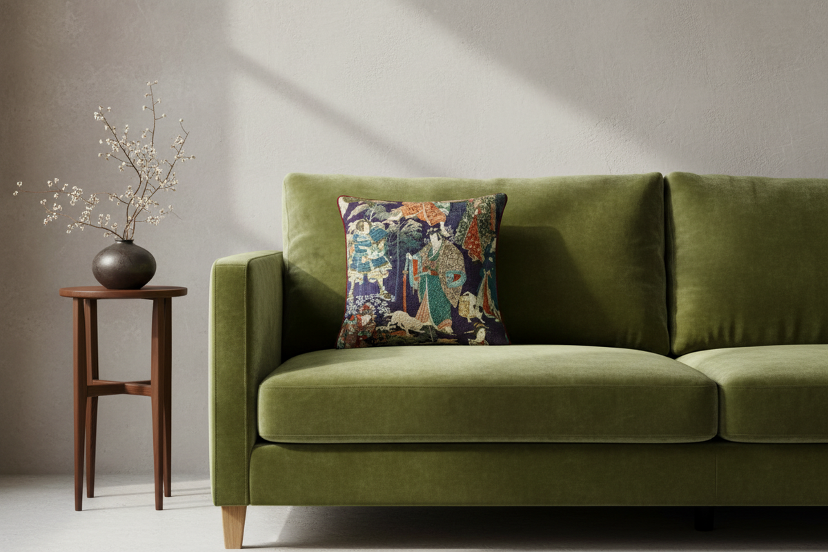 An olive green velvet sofa in a styled room setting, featuring a decorative throw pillow with a colorful Japanese ukiyo-e woodblock print and a small wooden side table with dried branches on a textured light gray wall.