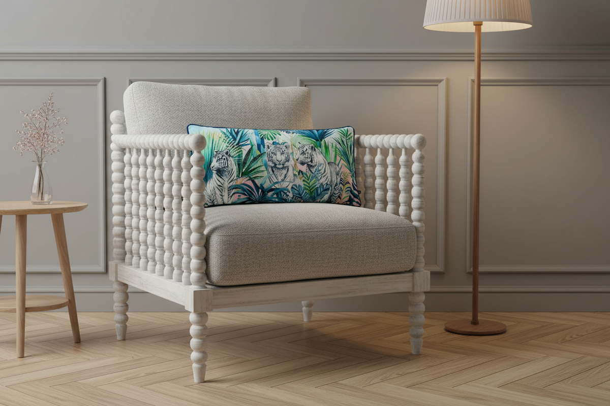 A white upholstered armchair with a beaded spindle frame and a colorful tropical leaf throw pillow, set in a styled room with a wooden floor, a side table, and a floor lamp.