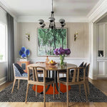 Stylish dining room featuring the Abstract Maze Orange Sun Hand Tufted Wool Rug, an area rug with a bold geometric pattern in black and orange. Perfectly suited for living room and dining room spaces, this wool rug adds a vibrant touch under the wooden dining table and chairs, enhancing the elegance of the dining room area.