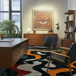 A stylish living room featuring an Abstract Whisker Hand Tufted Area Rug. The wool rug, perfect for dining rooms and living spaces, showcases a bold design in black, white, red, and orange. It adds a sophisticated touch under a modern dining table setup with wooden furniture and a large window view.