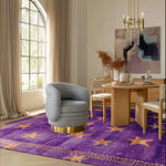 Elegant living room showcasing an Arabian Nights hand tufted area rug with a vibrant purple and gold star pattern. This luxurious wool rug enhances the cozy atmosphere, beautifully complementing the modern furniture and spacious window, ideal for any living room or bedroom decor.