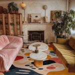 A cozy living room featuring a colorful Arched Adventures Hand Tufted Area Rug, perfect for adding a touch of modern flair. This contemporary wool rug serves as a stunning centerpiece, complementing the pink and yellow sofas. Ideal for use as a bathroom runner rug, kitchen runner rug, or large living room rug, its vibrant abstract patterns bring warmth and style to any space.
