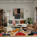 Stylish living room featuring an Arched Adventures Hand Tufted Area Rug with a bold abstract design. The wool rug, perfect for large living rooms, adds a contemporary touch with its vibrant colors. The room includes a white sofa, patterned cushions, a modern coffee table, and lush greenery, creating a cozy yet sophisticated ambiance.