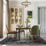 Elegant dining room featuring an Autumnal Forest Hand Knotted Area Rug with rich, earthy tones. The rug complements a round wooden table and upholstered chairs, creating a cozy and stylish atmosphere.