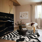 A stylish black and white melting hand-tufted wool area rug enhances a modern living room setting. The large living room rug features an abstract pattern, complementing a cozy, neutral-toned space with a sleek black coffee table and a comfortable armchair. Perfect for both offices and living rooms, this rug adds a touch of elegance and warmth.