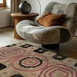 A cozy living room showcasing a Blossom Mandala Hand Tufted Area Rug with intricate pink and black circular patterns, perfect for adding warmth to any dining room or living area. The wool rug complements the stylish patchwork chair and wooden side table, creating an inviting and elegant atmosphere.