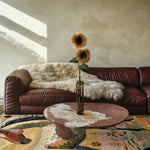 A cozy living room featuring a Bright Meadow Steed Hand Knotted Area Rug with a vibrant abstract design. This large square area rug adds a touch of elegance to the space, complemented by a plush leather sofa and a round coffee table. Perfect for those seeking a Persian-style wool rug for their living room.