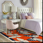 A vibrant Butterfly Meadow Hand Tufted Area Rug adds a splash of color to a stylish living room. The wool rug features large butterfly and leaf patterns in bold hues, perfectly complementing the elegant decor with a white desk, plush chair, and cozy bed. Ideal for both office spaces and living areas, this rug enhances any room with its artistic design.