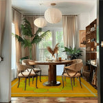 Stylish dining room featuring a Circle of Suns Square Hand Tufted Wool Rug in orange. The area rug adds a vibrant touch to the space, complementing the wooden dining table and chairs. Natural light streams in through large windows, highlighting the wool rug's unique circular design, perfect for both living room and dining room settings.