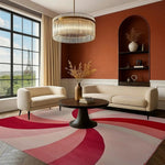 A stylish living room featuring a Crimson Swirl Hand Tufted Area Rug in an 8x10 size. The wool rug's vibrant red and pink abstract pattern enhances the room's modern decor, complementing the neutral-toned sofas and a chic round coffee table. Large windows bring in natural light, perfect for showcasing living room area rugs.