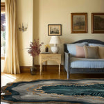 Stylish living room featuring the Crystal Depths Hand Tufted Viscose Area Rug with an abstract design in serene blue and gray tones. The rug complements the elegant decor with a vintage sofa, wooden side table, and tasteful wall art.