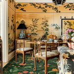 A beautifully decorated living room featuring the Emerald Garden Hand Tufted Rug. This elegant area rug, perfect for large living rooms, showcases a lush green background with vibrant floral patterns. The wool rug complements the room's warm, sophisticated decor, including wooden chairs and a decorative wall mural.