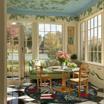 A vibrant living room featuring a Festive Whimsy Round Hand Tufted Area Rug with an abstract pattern. This wool rug adds charm to the room with its bold colors, complementing the green sofa and wooden chairs. Large windows let in natural light, highlighting the elegant round rug, perfect for living room decor.