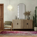 A contemporary wool runner rug with vibrant pink and neutral tones lies elegantly on a wooden floor. Its abstract design adds a modern touch, perfect for spaces like offices, kitchens, or hallways. The stylish setting includes a wooden cabinet, a chic chair, and a decorative mirror, enhancing the area rug's appeal.