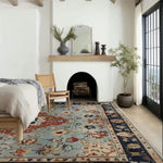 A beautifully styled living room featuring a Floral Cascade Blue Hand Knotted Area Rug. The vintage square area rug displays intricate Persian-inspired designs in shades of blue and red, perfect for enhancing large living room spaces. Its wool texture adds a touch of elegance and warmth to the room, complementing the modern decor and natural light pouring through the windows.