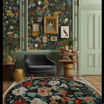 The Garden Whispers Hand Tufted Rug adds a touch of elegance to a formal dining room, featuring a vibrant floral design in rich colors. This wool rug serves as a stunning square area rug, perfect for dining rooms or living rooms. Set against a backdrop of a tastefully decorated wall with vintage paintings and a cozy armchair, this rug enhances the charm of your home decor.