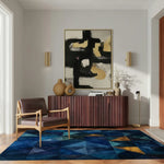 A contemporary living room setting featuring the Geometric Getaway Hand Tufted Wool Rug. This vibrant area rug, ideal for kitchen rugs or hallway runner rugs, boasts a striking pattern with rich blue and gold tones. Perfect for adding a touch of elegance to your living room, this wool rug complements the modern decor, including an abstract painting, a stylish armchair, and a wooden sideboard.