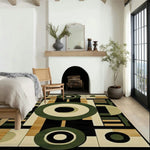 A contemporary wool rug with geometric patterns in green, beige, and black complements a cozy dining room setting. This large area rug adds a modern touch to the space, featuring a stylish arrangement of furniture and a fireplace.