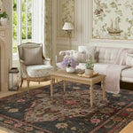 Living room with floral-patterned wallpaper, armchair, sofa, hand knotted pink and gray rug, and a coffee table.