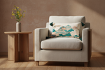 A beige upholstered armchair with woven cane side panels and white legs, styled in a bright room with a decorative multicolor landscape throw pillow, a patterned cream pillow, a gold floor lamp, and a wooden side table with pink flowers.