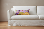 A white slipcovered sofa in a minimalist room setting, featuring a colorful rectangular lumbar pillow with a purple, yellow, and green floral pattern.