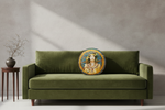 A round decorative throw pillow with an ornate Art Nouveau illustration of a woman, displayed on a white slipcovered sofa in a minimalist room setting.