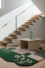 Modern staircase with a table and decorative green tufted rug in a well-lit room.