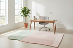 Modern home office with a desk, chair, laptop, and plant on a pink and green and pink contemporary rug.