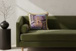 A brown leather armchair in a styled living room setting, featuring a decorative throw pillow with a gold chandelier design, a brass floor lamp, and a small side table with white flowers.