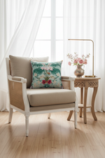 A white upholstered armchair with turned spindle-style arms and legs, styled in a room with gray paneled walls, a lit floor lamp, a small side table with greenery, and a floral accent pillow.