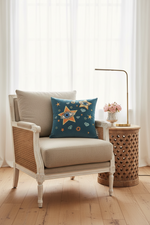 A brown leather armchair in a styled room corner with a blue throw pillow featuring a star pattern, a floor lamp, and a side table with flowers.