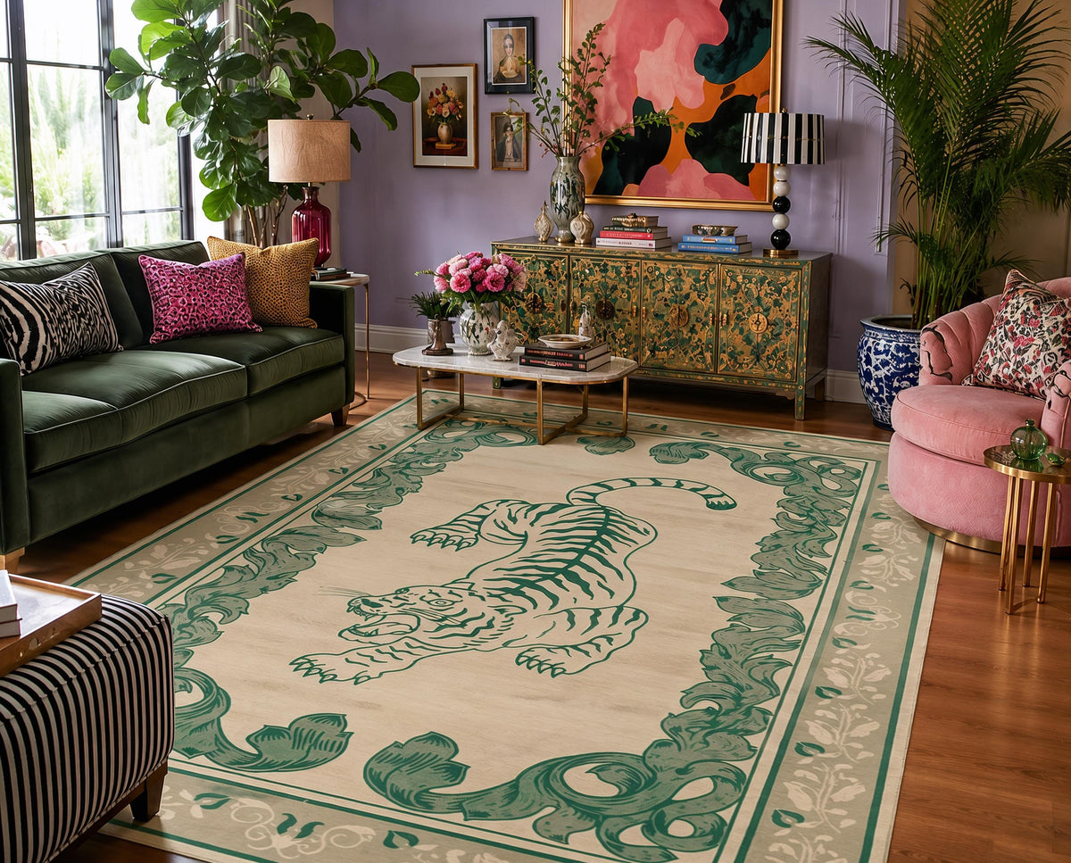 A large rectangular area rug with a cream background and a green tiger and scroll border, shown in a styled living room with a green sofa, pink armchair, cabinet, and plants.