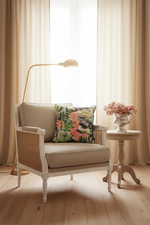 A light gray upholstered armchair with a colorful tropical floral pillow, set in a styled room with a wood-paneled wall, a floor lamp, and a small side table.
