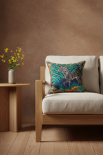 A square throw pillow with a colorful zebra print on a teal and blue background, styled on a light wood armchair in a modern living room setting.
