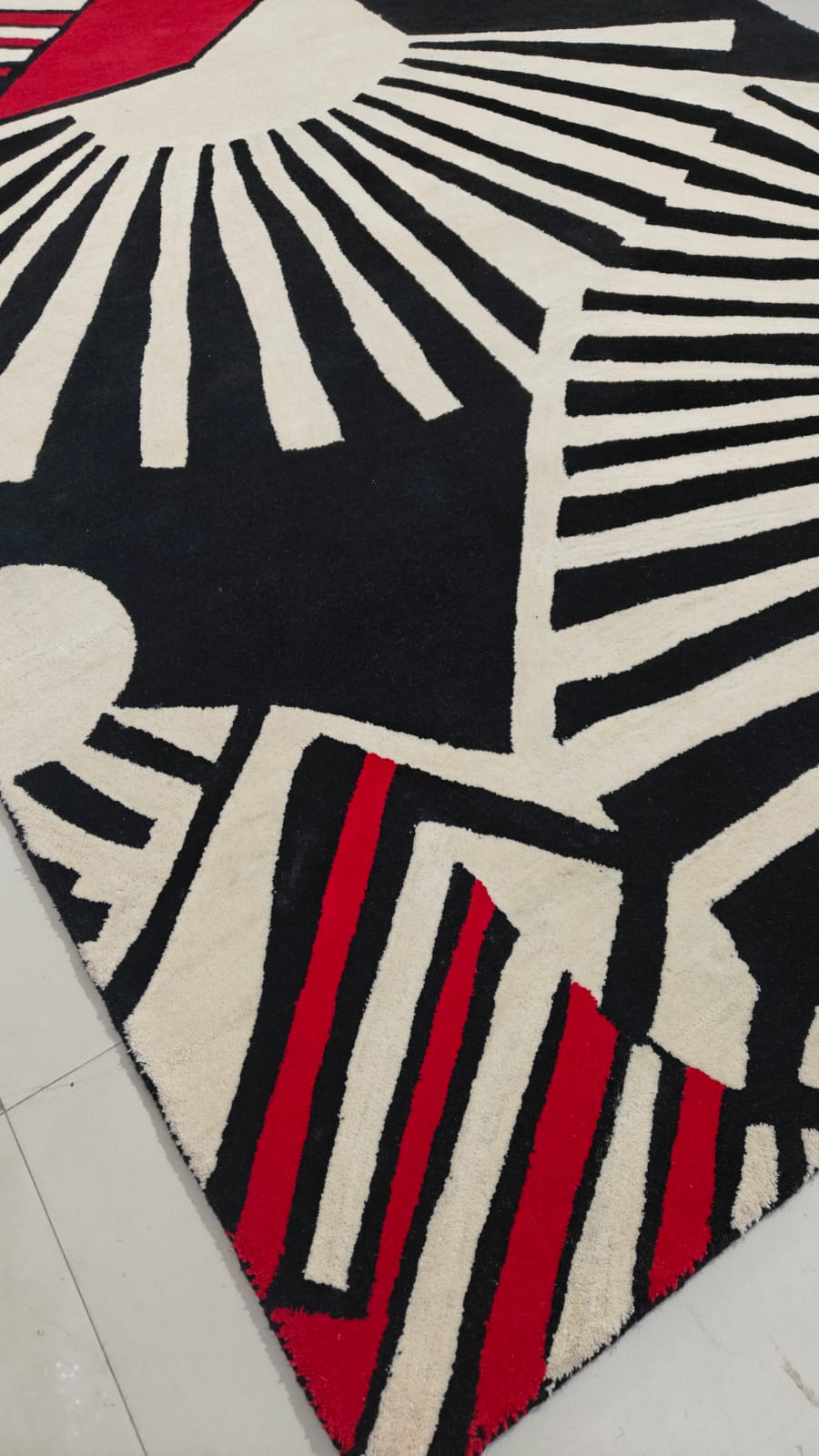 Geometric patterned rug with black, white, and red design on a light wood floor.