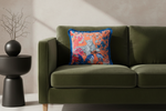 A square decorative throw pillow with a vibrant orange and blue Japanese-style floral print featuring a white tiger, styled on an olive green velvet sofa next to a black side table.