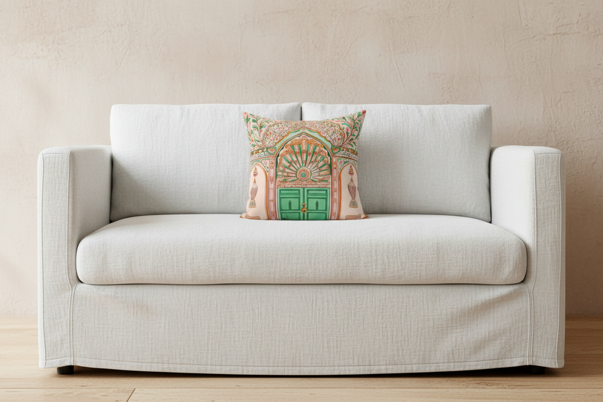 A light beige slipcovered loveseat sofa with a decorative throw pillow featuring a colorful architectural arch design, set against a textured beige wall and light wood floor.