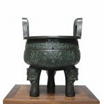 Bronze tripod pot on a wooden platform with Chinese text on a gray background