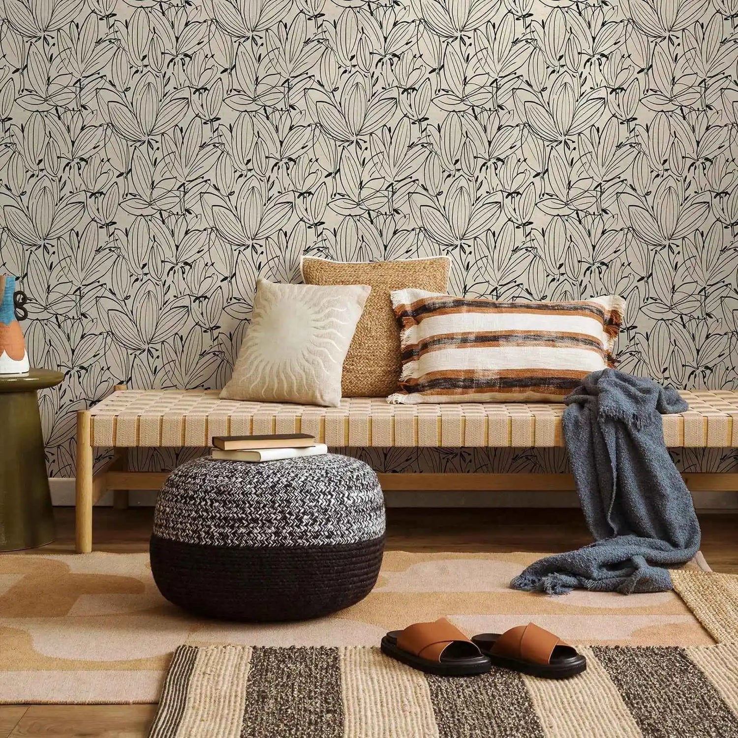 Living room with a bench, ottoman, and pillows against a patterned wall.